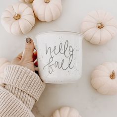 a person holding a coffee mug with the words hello fall written on it next to pumpkins