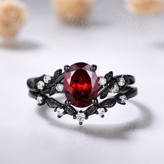 a ring with a large red stone surrounded by small white stones and black metal leaves