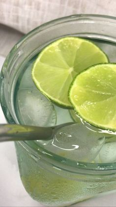 two limes are sitting on top of the ice in a glass jar with water