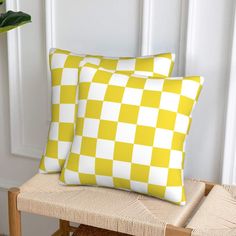 two yellow and white checkered pillows sitting on a bench next to a potted plant