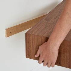 a person is reaching for something on the edge of a wooden shelf that's attached to a wall