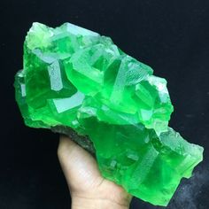 a hand holding a rock with green crystals on it