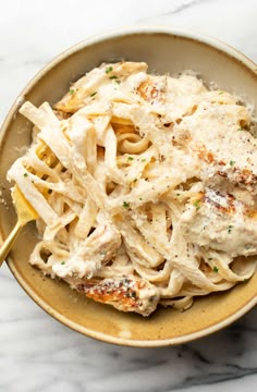 a bowl filled with pasta and sauce on top of a marble countertop next to a wooden spoon