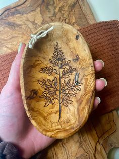 a hand holding a wooden bowl with a tree etched on it