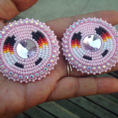 a pair of pink and black beaded earrings on someone's hand with their fingers