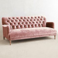 a pink velvet couch sitting on top of a white floor