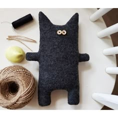 a cat made out of felt sitting next to some twine and spools of yarn