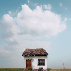 a small white house sitting on top of a grass covered field next to a body of water