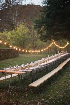 a long table set up with candles and place settings for an outdoor dinner in the woods