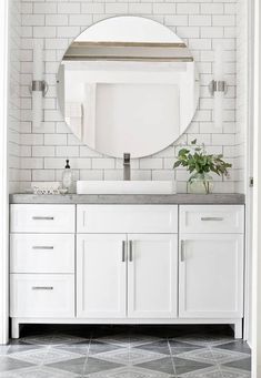 a bathroom with white cabinets and a round mirror