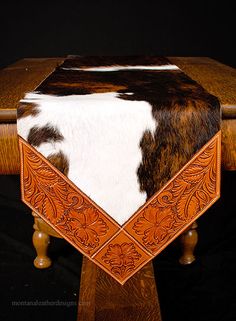 a cowhide and leather table runner on top of a wooden table with black background