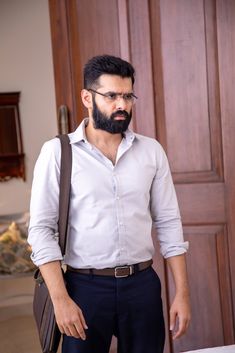 a man with a beard and glasses standing in front of a door