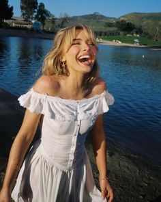 a woman in a white dress laughing by the water