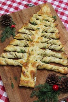 a christmas tree shaped pizza on a wooden cutting board with pine cones and evergreens