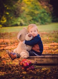 a little boy sitting on top of a wooden crate holding a stuffed animal in his arms