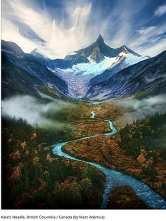 a river running through a lush green field next to tall snow covered mountain peaks in the distance