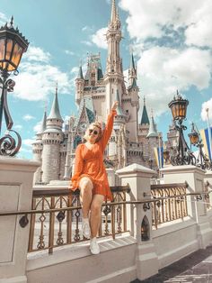 a woman in an orange dress is sitting on a railing near a castle and street lights