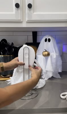 a person holding a paper towel in front of two ghost heads on a kitchen counter