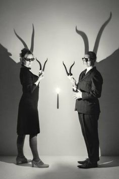 two people standing next to each other in front of a wall with scissors on it