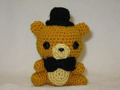 a crocheted teddy bear with a top hat and bow tie sitting on a white surface