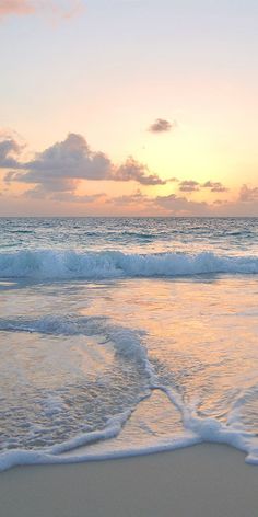 a beach with waves crashing on it and the sun setting in the sky above them