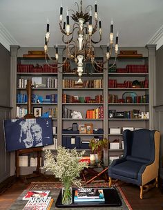 a living room filled with furniture and a chandelier hanging from the ceiling next to a bookshelf