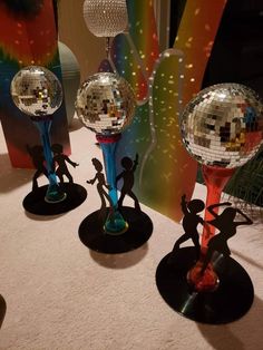 three mirrored disco balls on black bases with people dancing around them