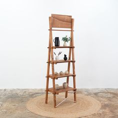 a wooden shelf with pots and vases on it in front of a white wall