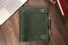 a green leather notebook sitting on top of a wooden desk next to a laptop computer