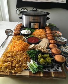 a wooden cutting board topped with different types of food next to a crock pot