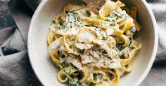 a person is holding a spoon over a bowl of pasta with chicken and spinach