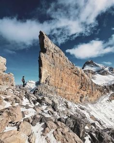 two people standing at the top of a mountain with snow on it and rocks below