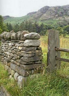 an old stone wall made out of rocks in the grass with mountains in the background