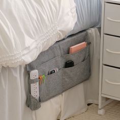 a bed with white sheets and a gray bag hanging on the headboard