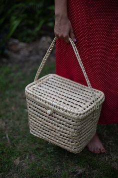 a woman is holding a wicker basket in her hand while standing on the grass