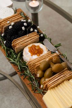 an assortment of cheeses, crackers and olives on a wooden platter