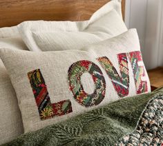 a close up of a pillow on a bed with the word love embroidered on it