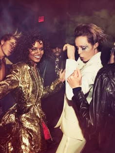 two women in gold and black outfits standing next to each other with their arms around one another