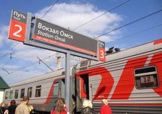 people are standing on the platform next to a red and gray train at an outdoor station