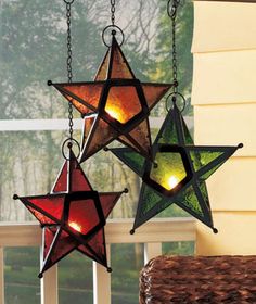 three stained glass stars hanging from chains on a window sill with lights in them