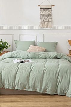 a bed with green comforters and pillows in a white room next to a potted plant