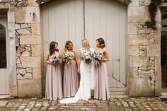 a group of women standing next to each other in front of a stone building holding bouquets