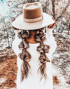 a woman with long braids and a hat on her head in the middle of a field