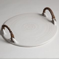 a white platter with two brown handles and rope around the rim, on a white surface