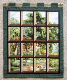 a quilted wall hanging on the side of a building with trees and houses in it