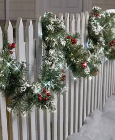 christmas wreaths hanging on a white picket fence