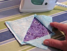 a hand is holding some fabric on top of a table with a sewing machine in the background