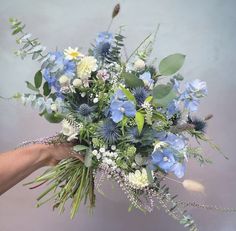 a bouquet of blue and white flowers being held by a woman's hand with greenery