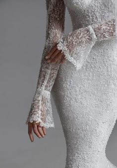 a woman wearing a white wedding dress with long sleeves and beading on the shoulders