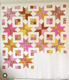 a quilted wall hanging on the side of a white wall with pink and yellow stars